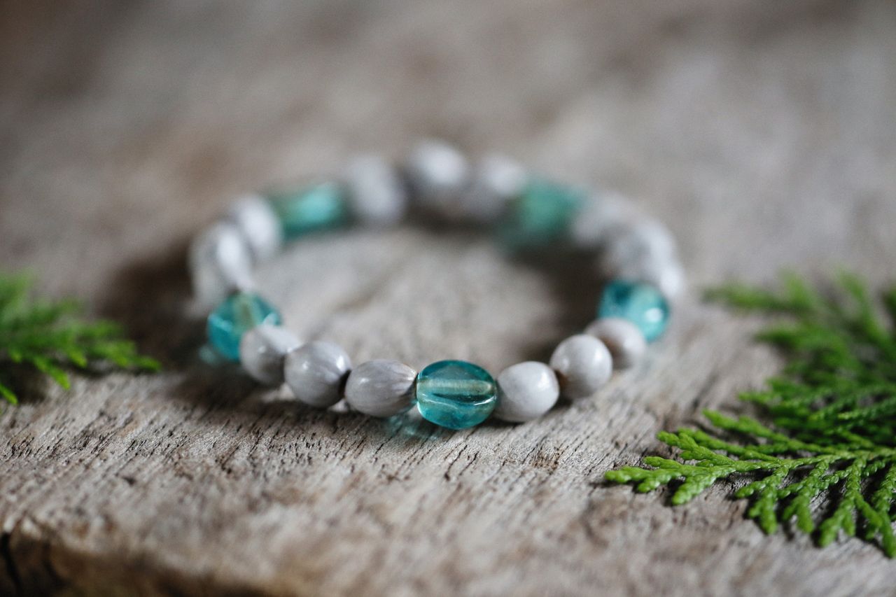 Elegant bracelet with turquoise glass and marble beads on rustic wood surface.