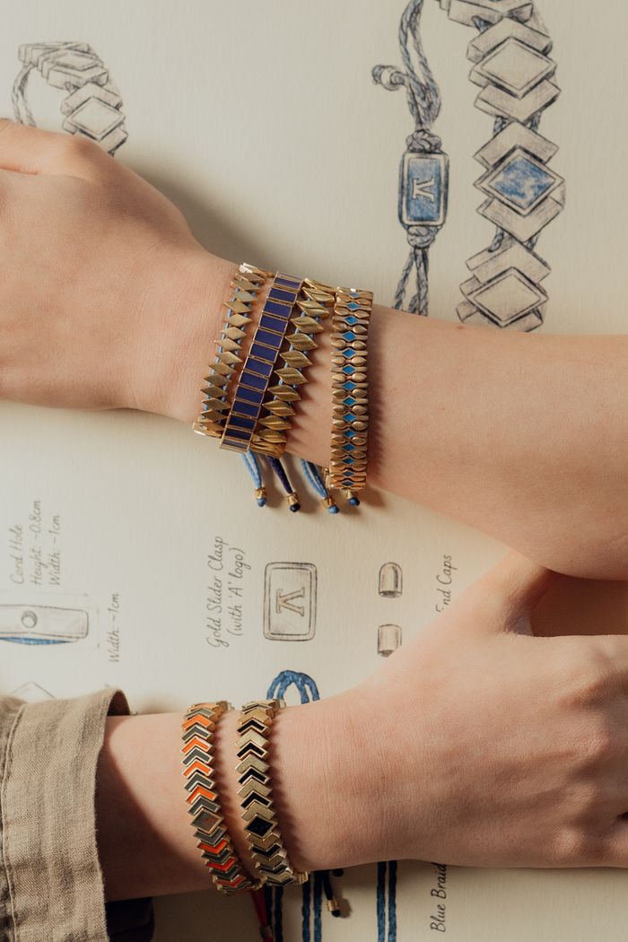 Close-up of artistic handmade bracelets on wrists against a jewelry design blueprint background.